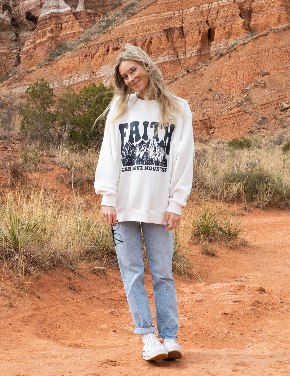 White crewneck sweatshirt with “Faith” mountain graphic and caption text on front