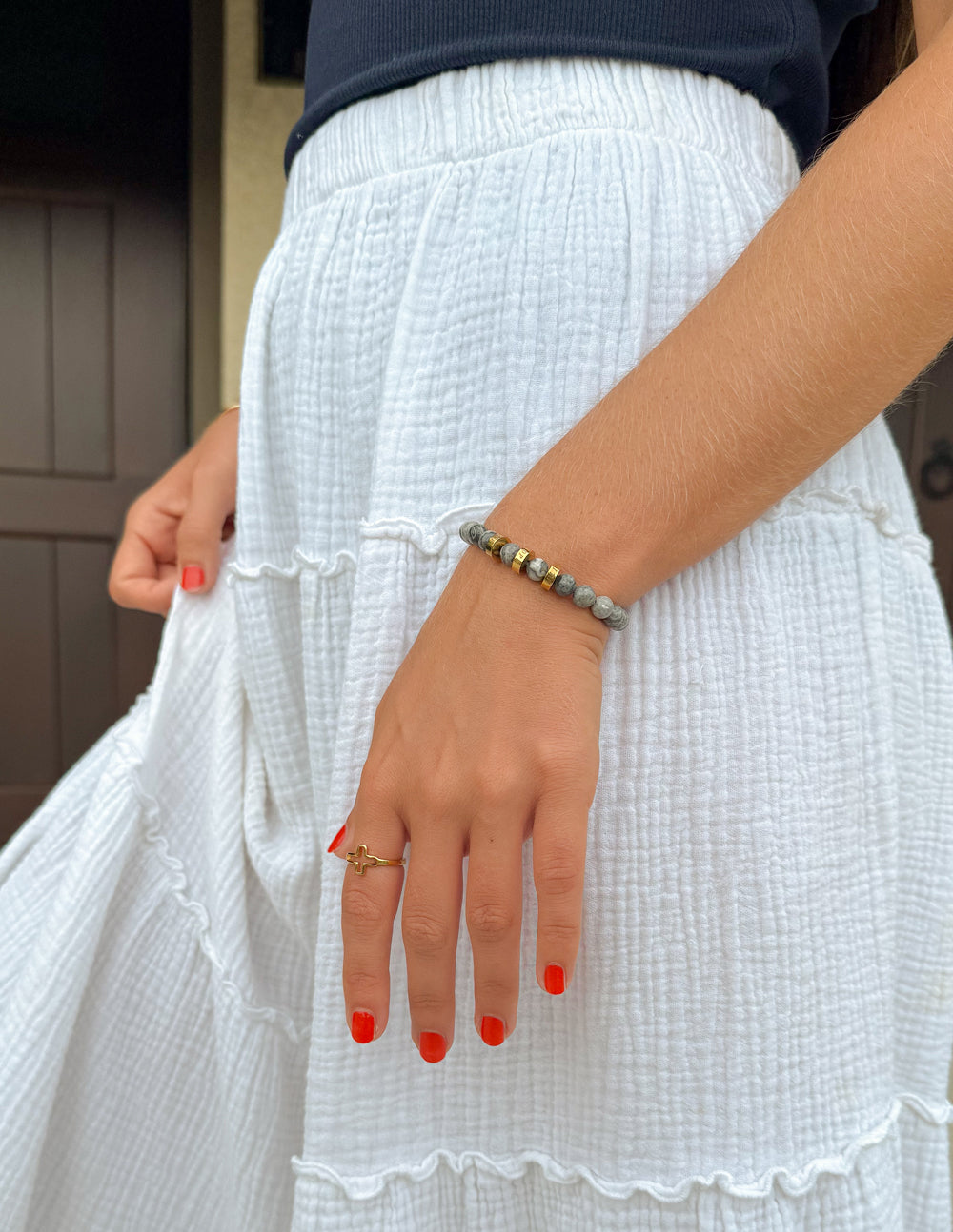 Gray stone bead bracelet with gold spacer beads on wrist over white dress