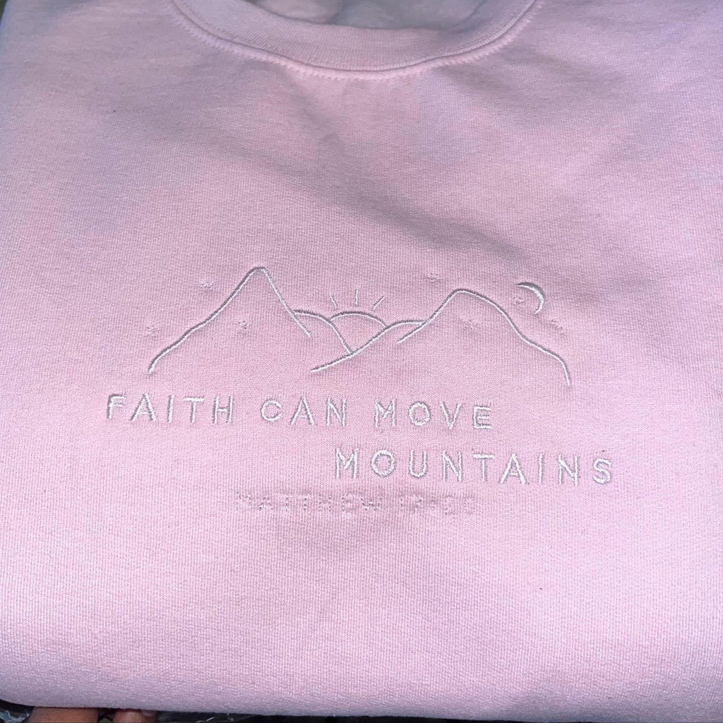 Light pink crewneck sweatshirt with embroidered mountain-and-verse design on chest