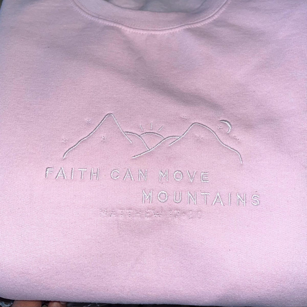Light pink crewneck sweatshirt with embroidered mountain-and-verse design on chest