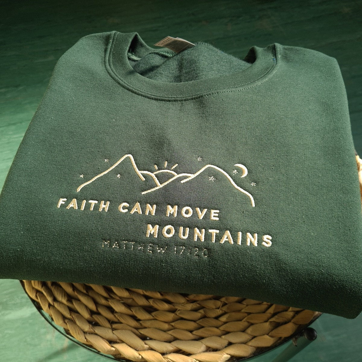 Dark green crewneck sweatshirt with embroidered faith and mountains verse at center
