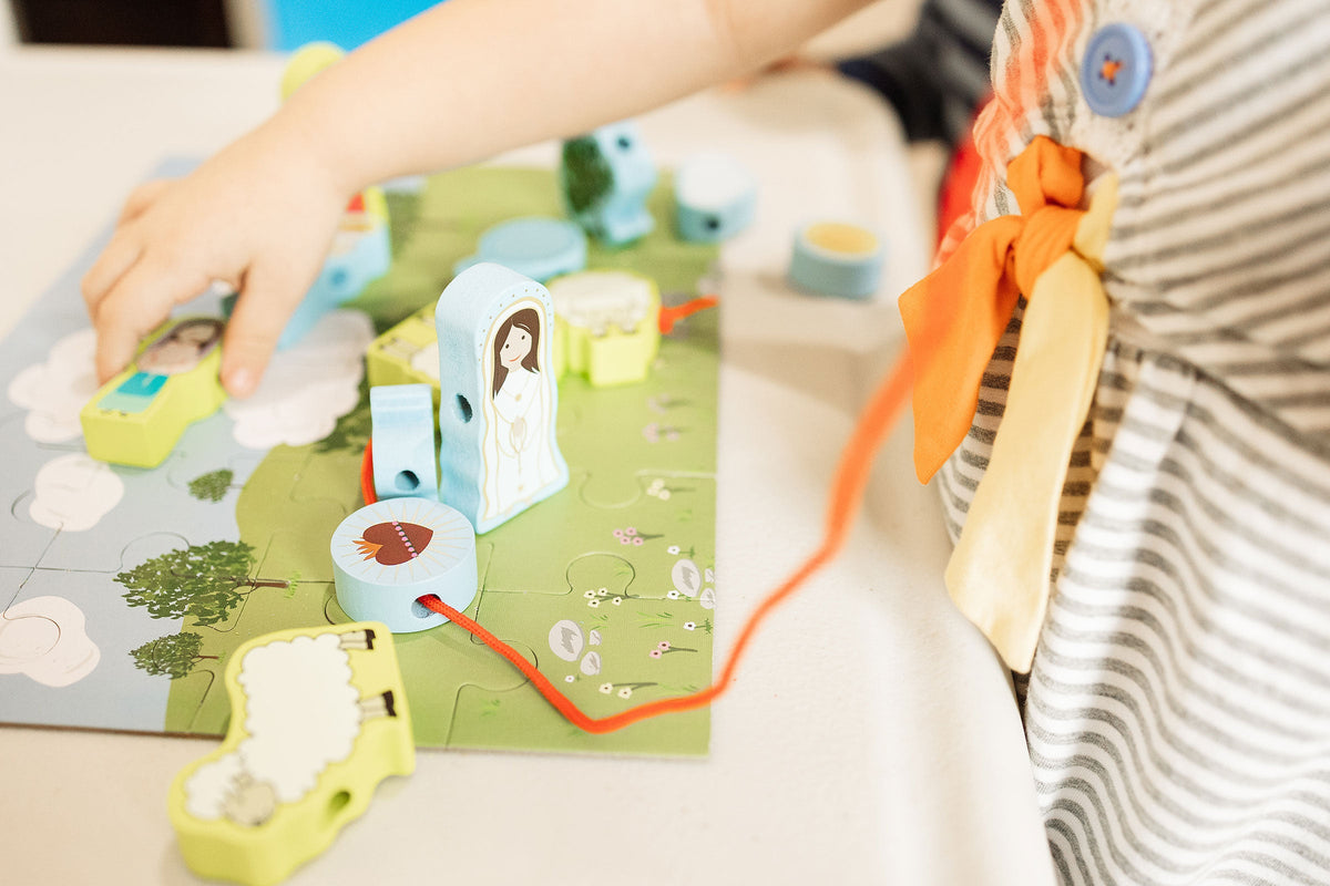 Child's hands placing pieces onto a lacing puzzle board with orange cords