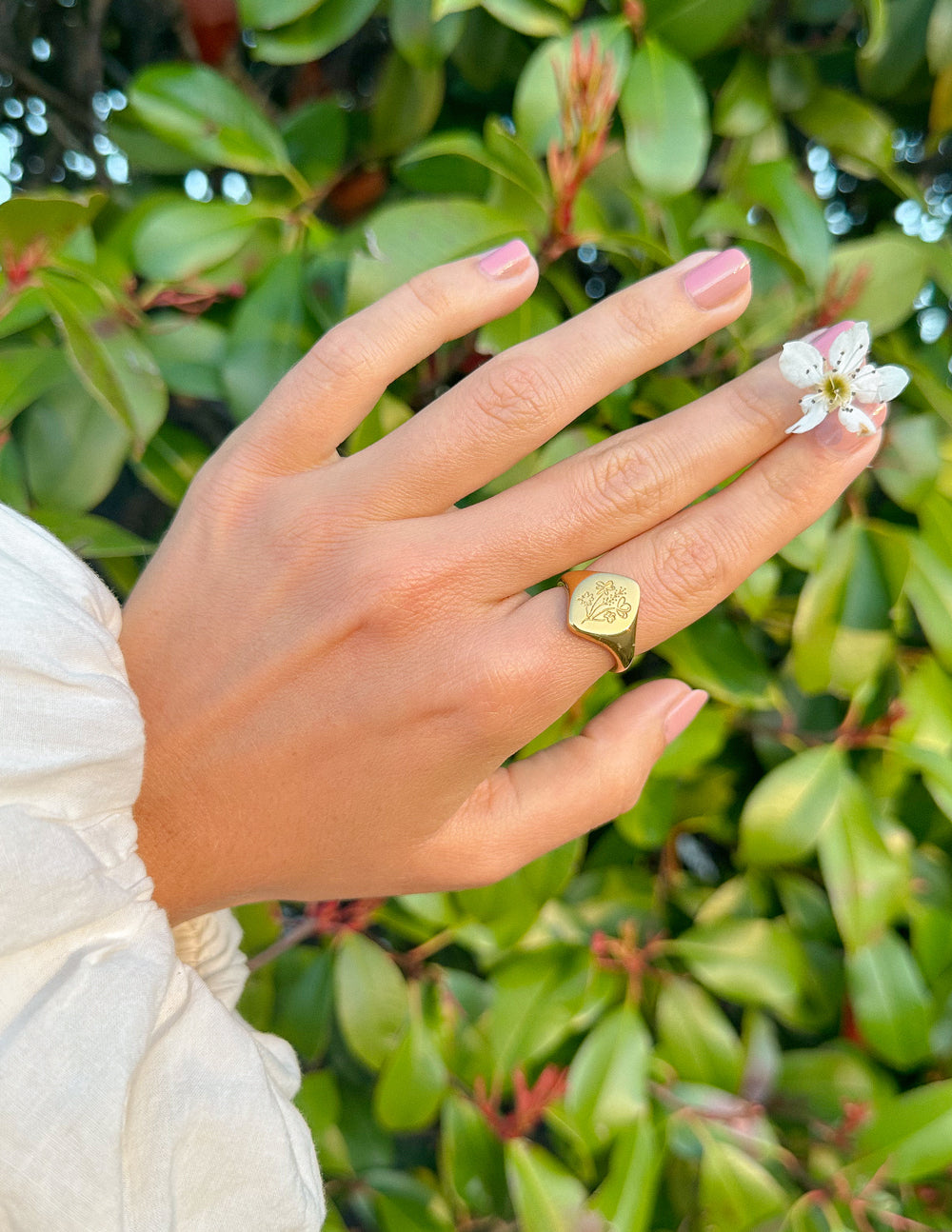 Gold-tone floral signet ring on finger, engraved flower-and-leaf design