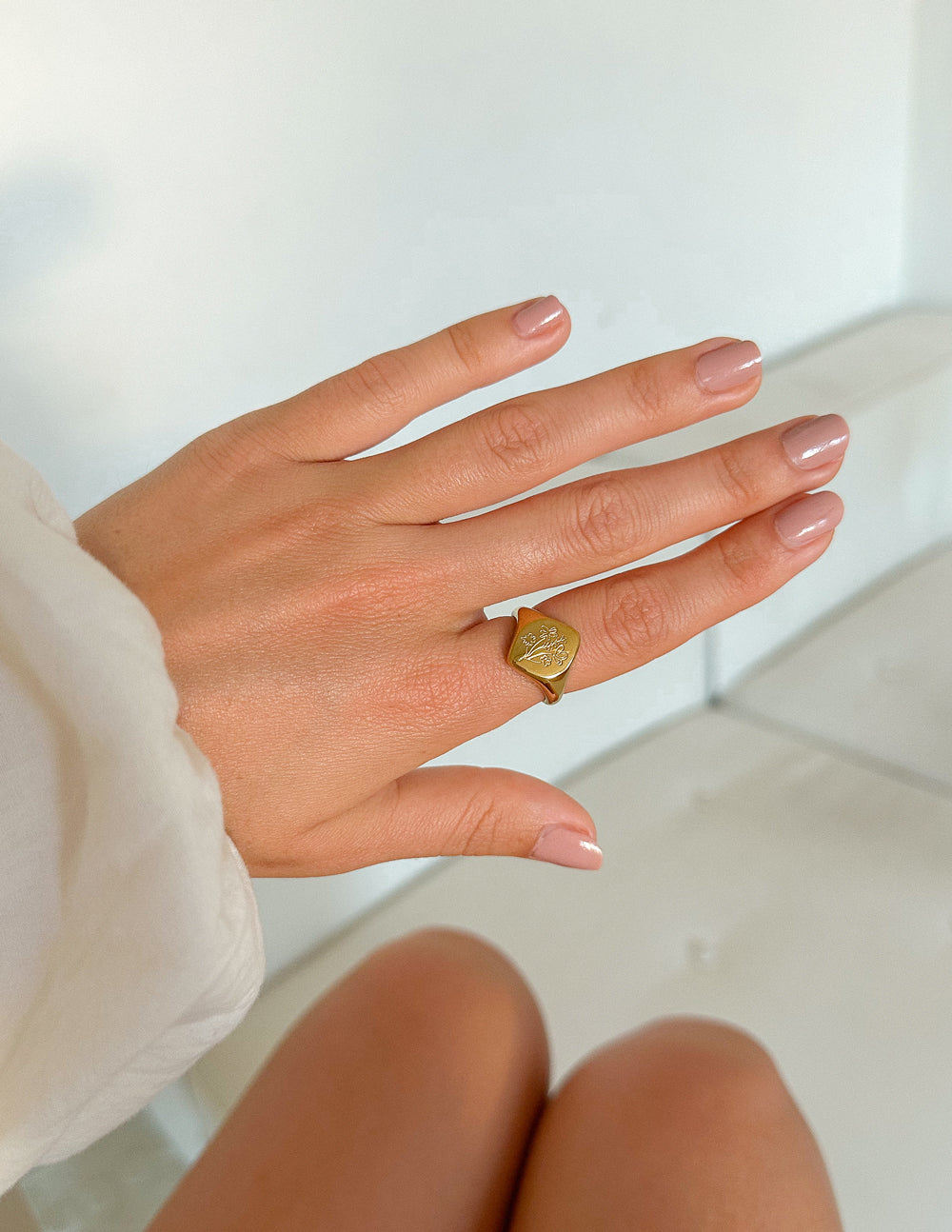 Gold-tone floral signet ring on finger with engraved floral emblem