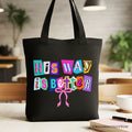 Black canvas tote bag with colorful 'His Way is Better' graphic and ribbon cross