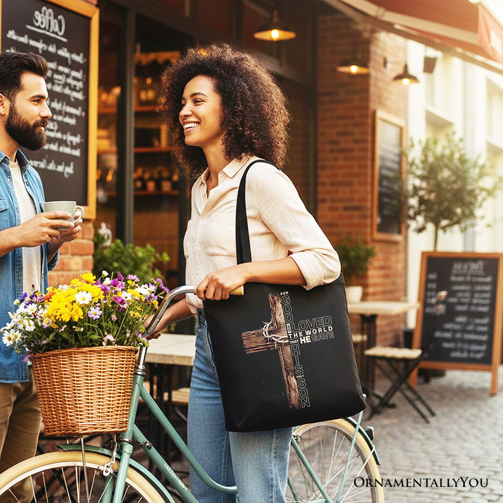 Black tote bag worn on shoulder with cross and quote print