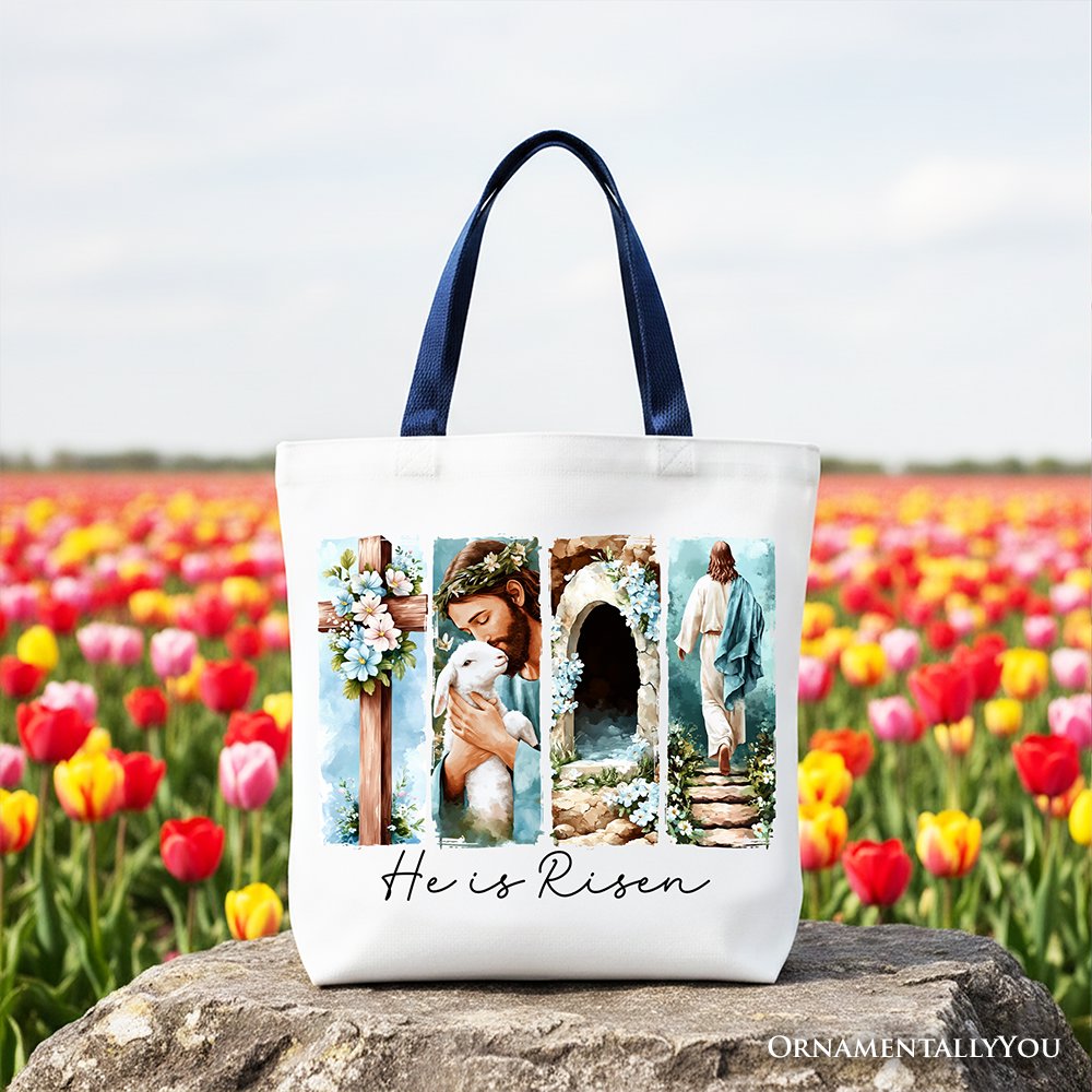 White canvas tote bag with navy handles and "He Is Risen" floral collage on front.