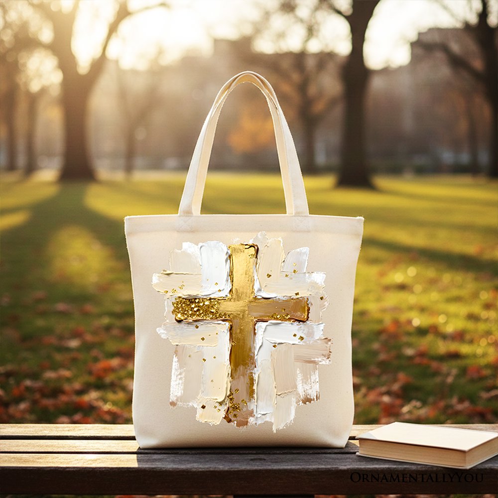 White canvas tote bag with gold cross front on outdoor bench