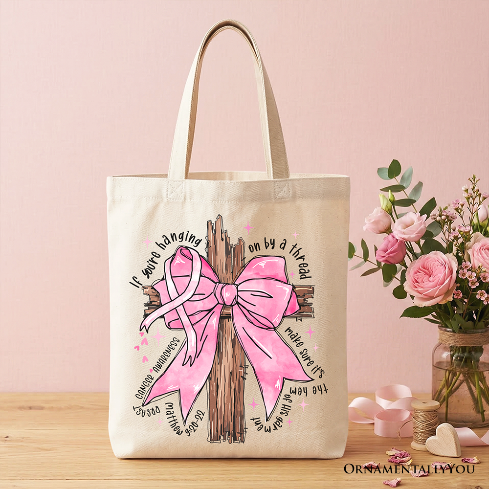 Beige tote bag with pink bow tree graphic, holds flowers nearby, handles up.