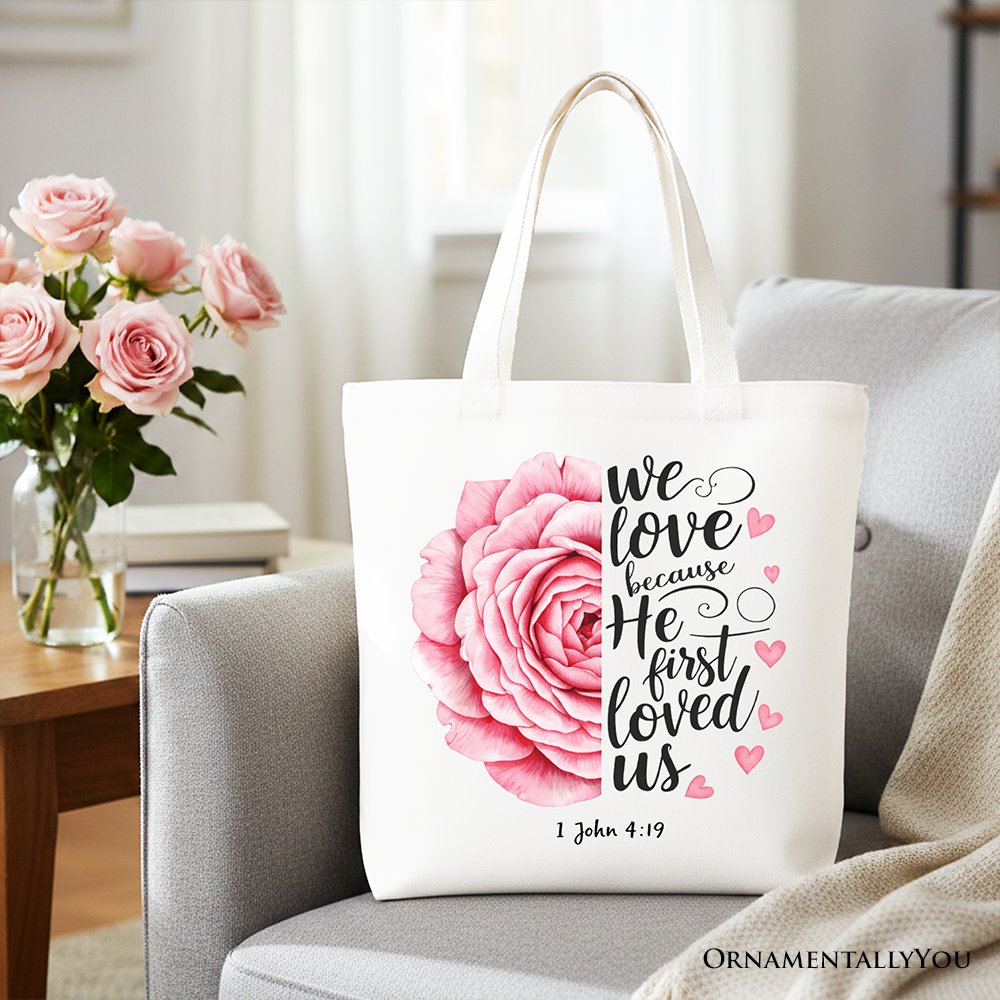 White tote bag with pink rose graphic and '1 John 4:19' text, light handles
