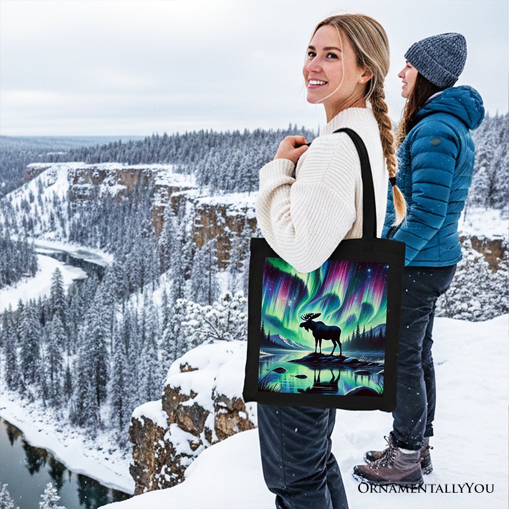 Black canvas tote bag with northern lights moose print, carried outdoors in snow