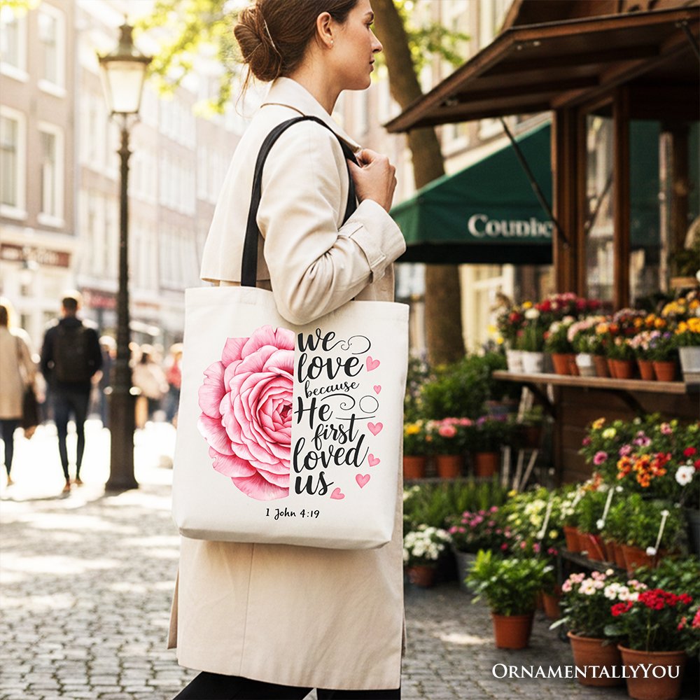White tote bag with pink rose and '1 John 4:19' text, dark handles