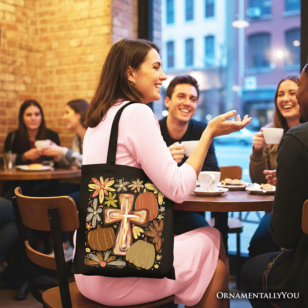 Black tote bag with gold cross and fall pumpkins graphic, carried by person