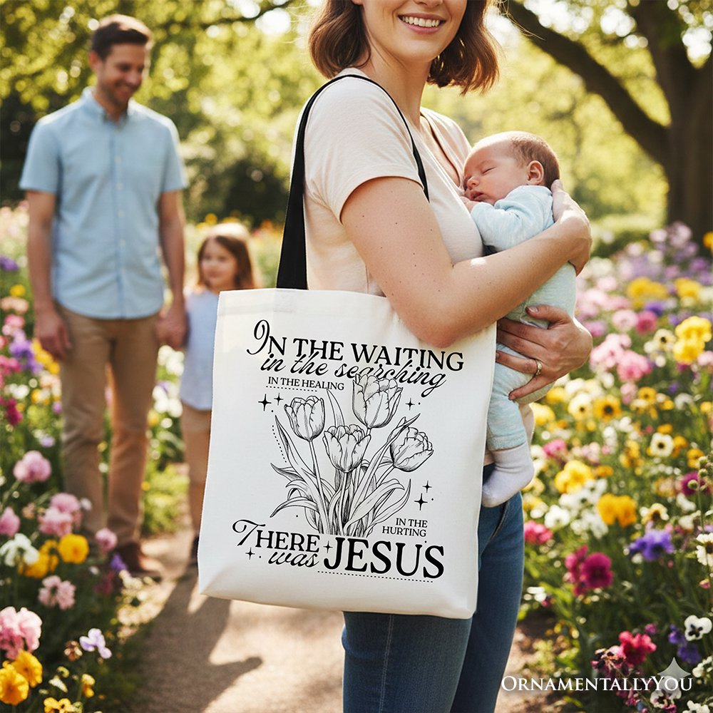 Cream tote bag with black handles and floral scripture print, carried by person holding baby