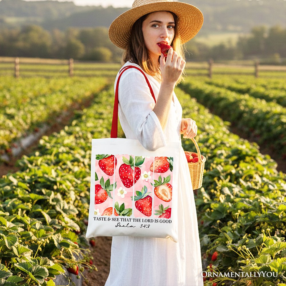 Strawberry print canvas tote bag held in hand with black strap handles