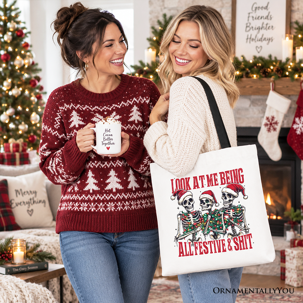 White cotton tote bag with skeleton holiday graphic and red slogan; held by two people