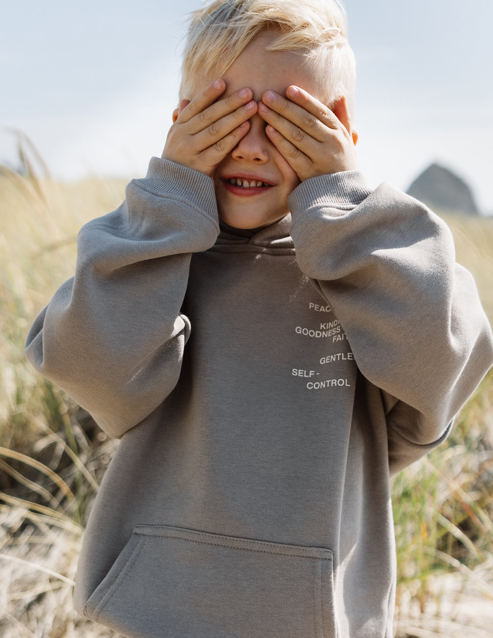 Kids gray hoodie with hood and chest print, child holding hands over eyes