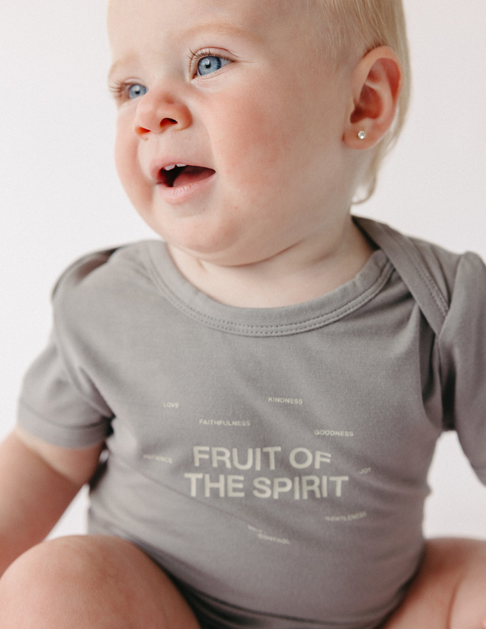 Taupe baby bodysuit close-up with 'Fruit of the Spirit' logo print