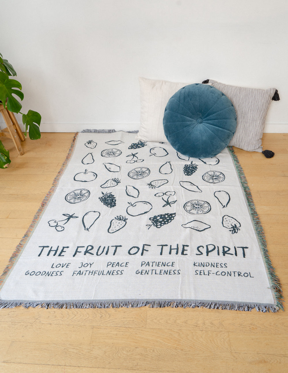 Cream throw blanket with black fruit icons, word bands, and tassel fringe