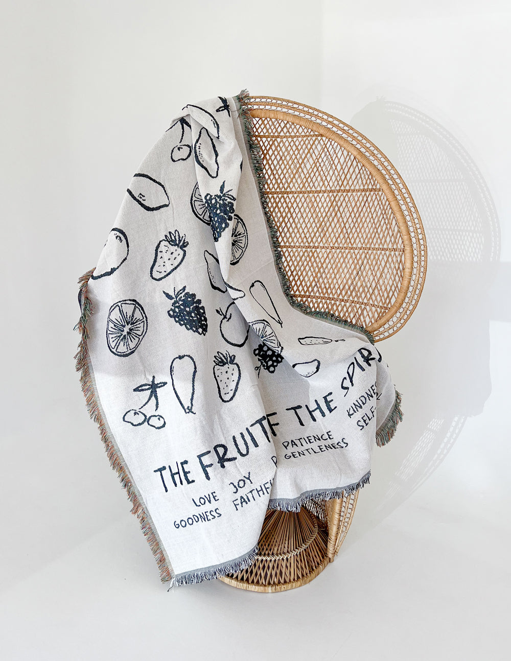 Cream throw blanket draped on chair with black fruit icons and fringed hem