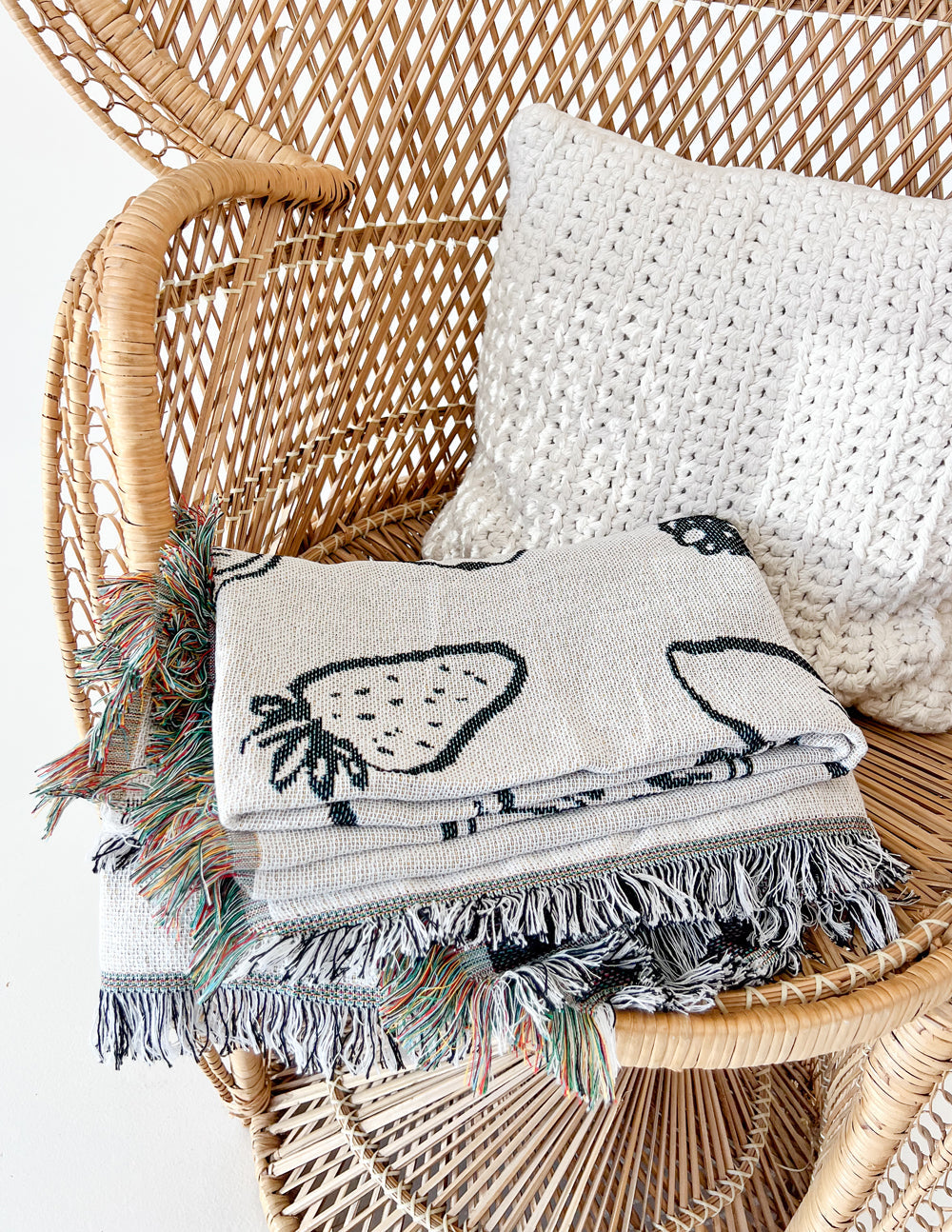 Folded cream throw blanket with black fruit icons and multicolor tassel fringe