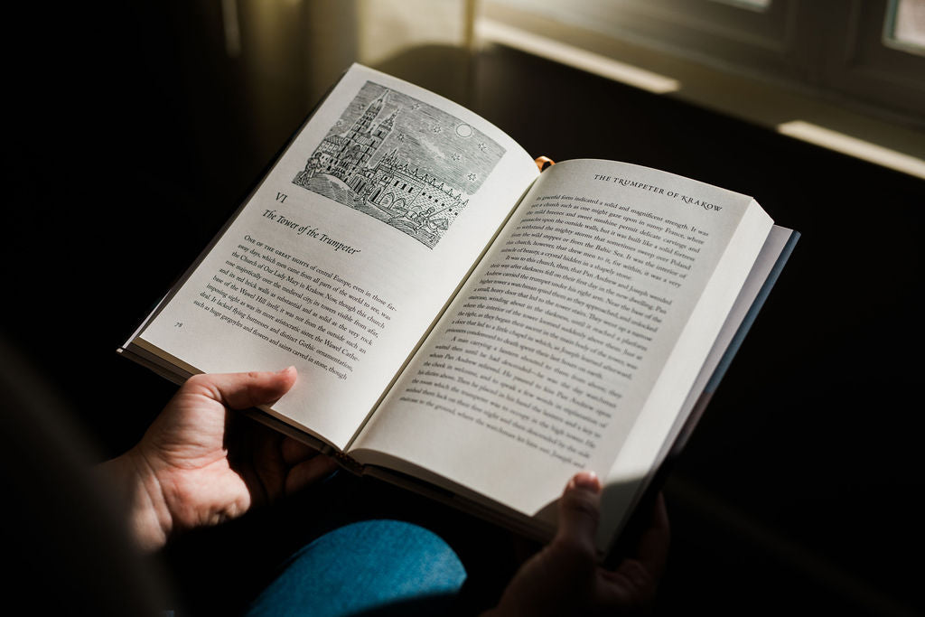 Open book held in hands with two-page spread of black text on a cream background.
