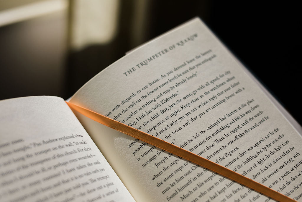 Open book pages with black text and an orange ribbon bookmark lying between lines.