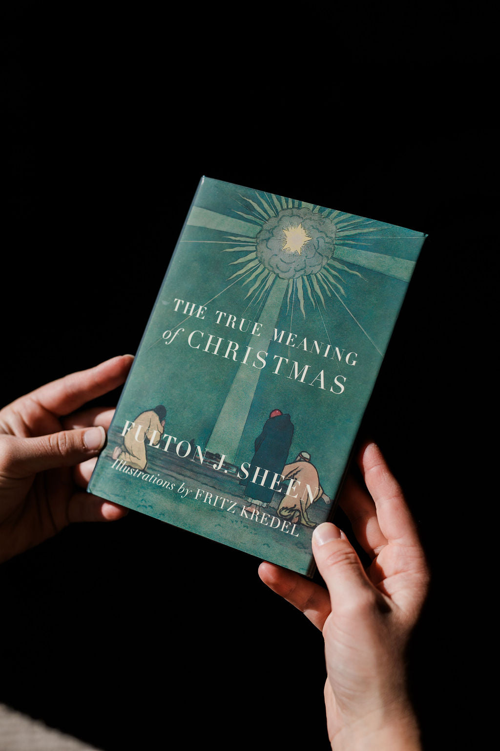 Christmas book held in hands, teal cover with sunburst illustration