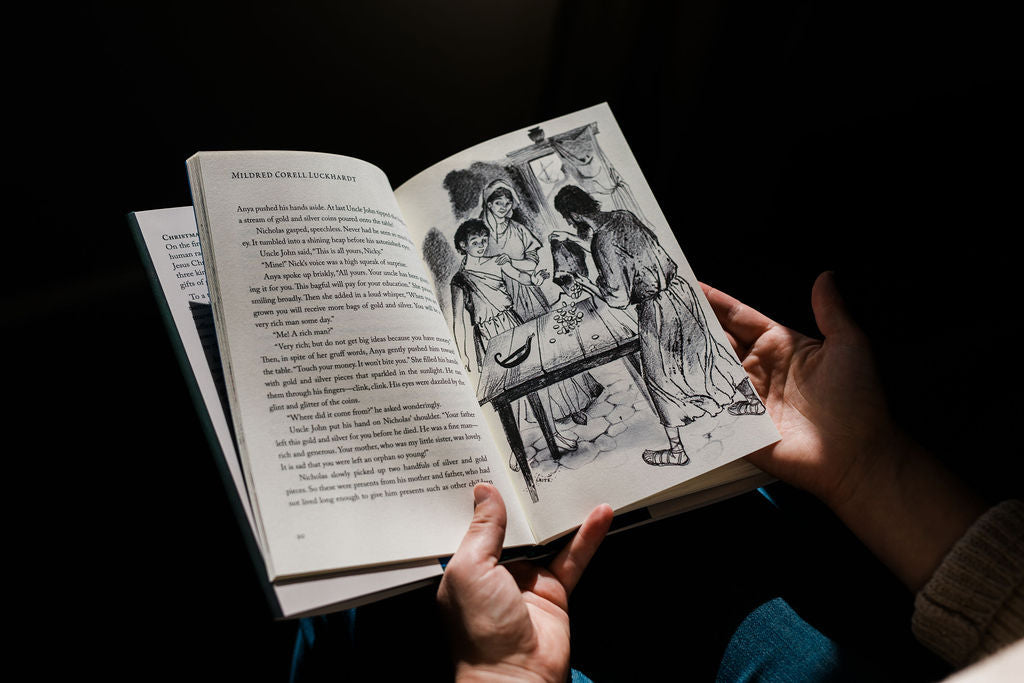 Open illustrated storybook with black-and-white scene and hands holding pages