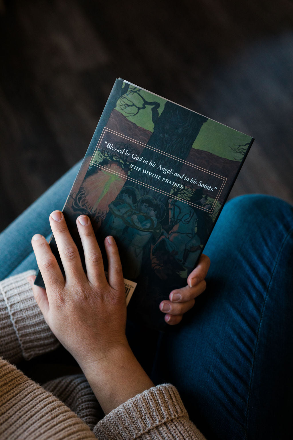 Saints book held on lap with blue-green cover and illustrated artwork
