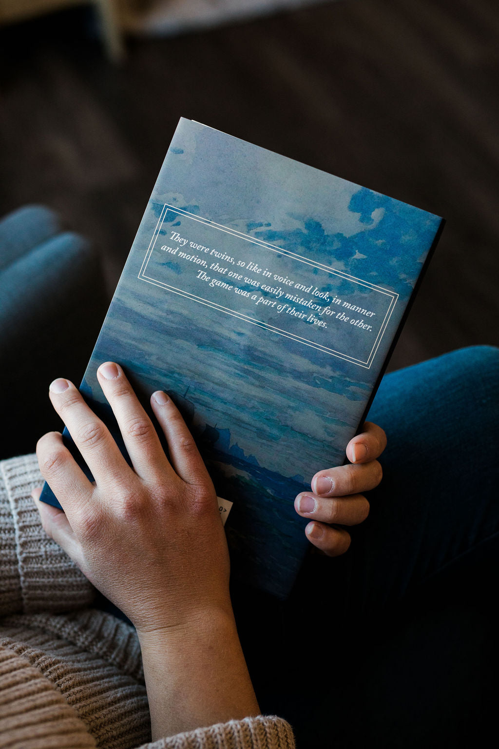 Blue ocean-toned hardcover book cover held on lap with both hands