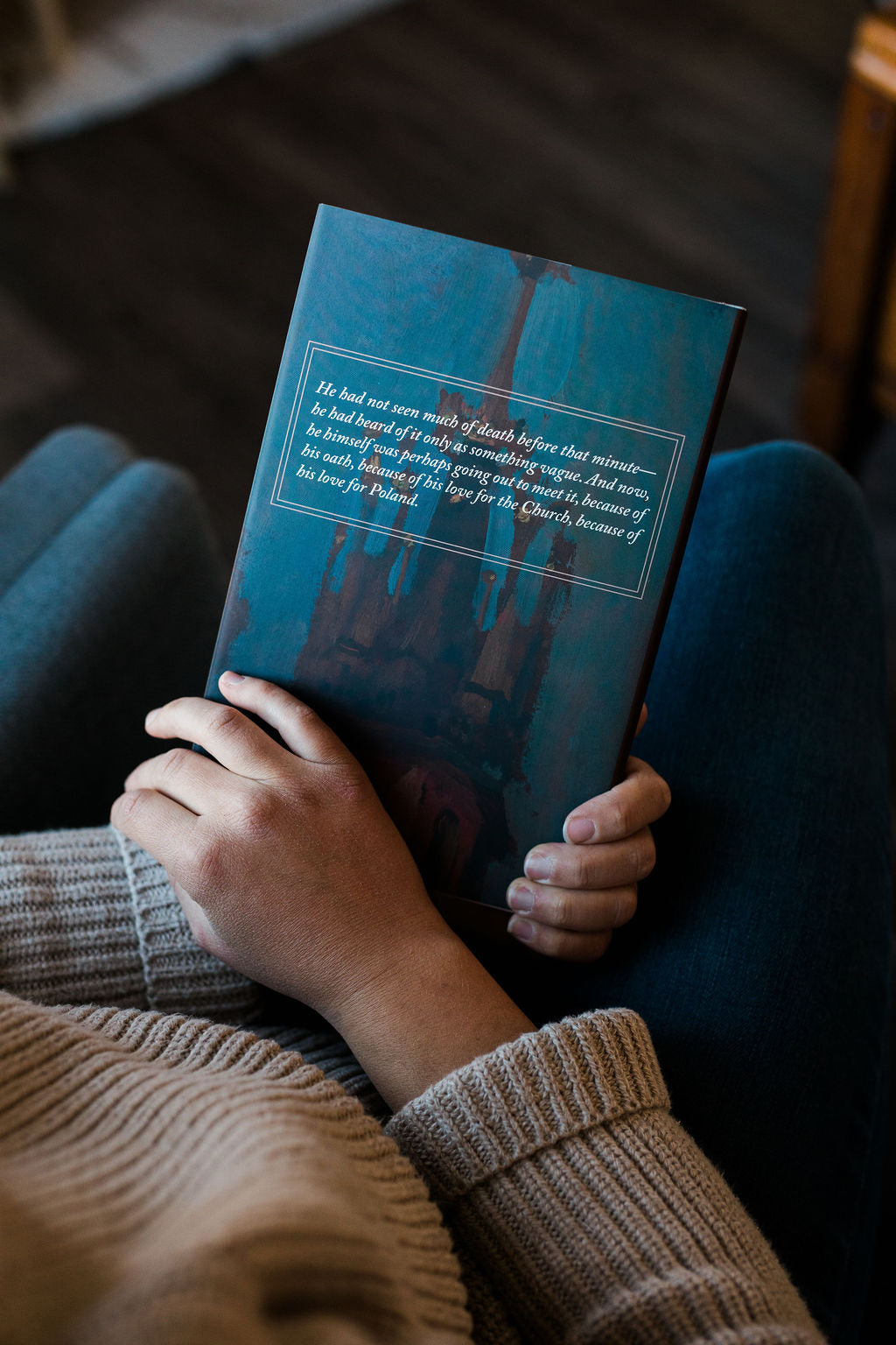 Hardcover book with blue cover held by two hands, gray text panel on back cover.