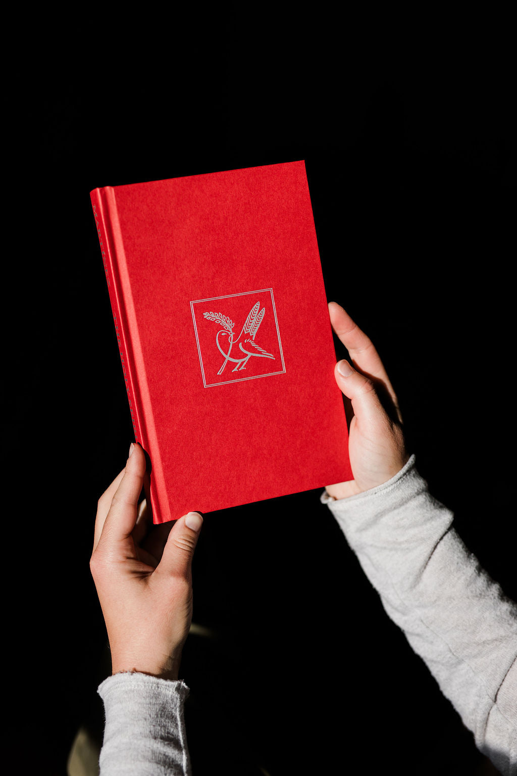 Red Holy Spirit book with small dove emblem on the cover, held in hands