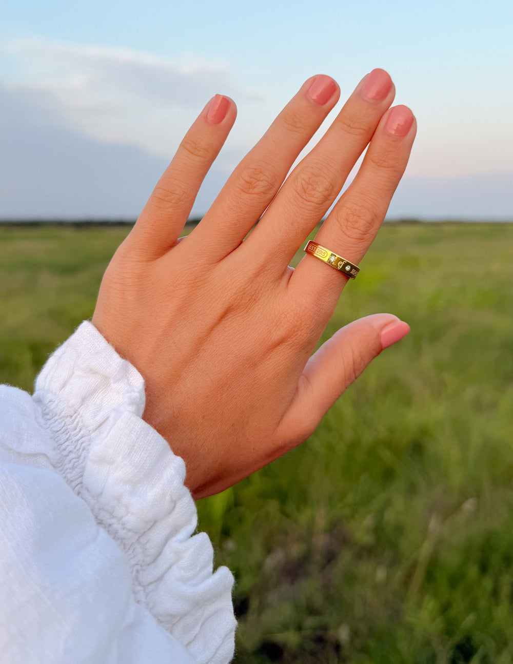 Gold-tone band ring with logo centerpiece and small gemstone details on finger
