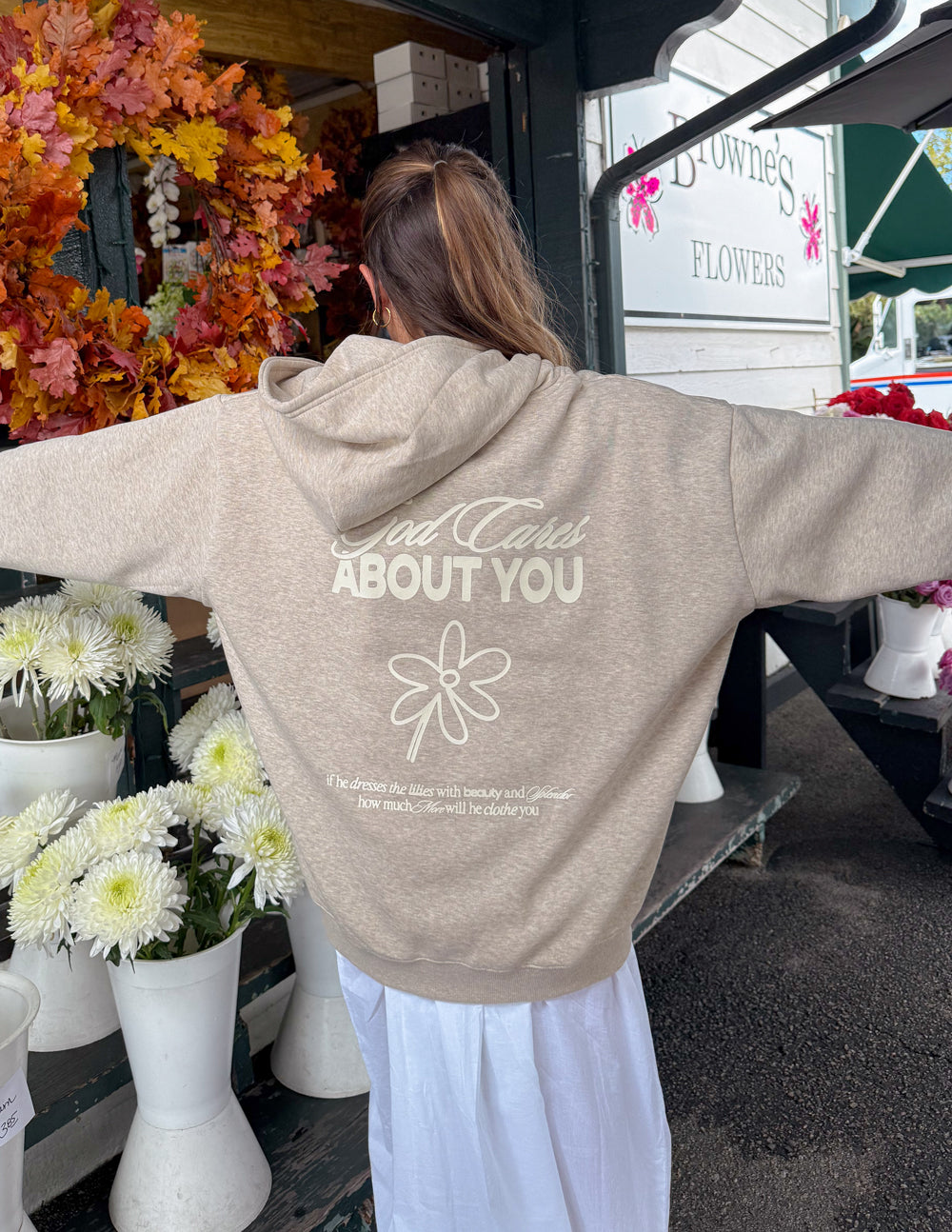 Light beige unisex hoodie back graphic with flower emblem and "ABOUT YOU"