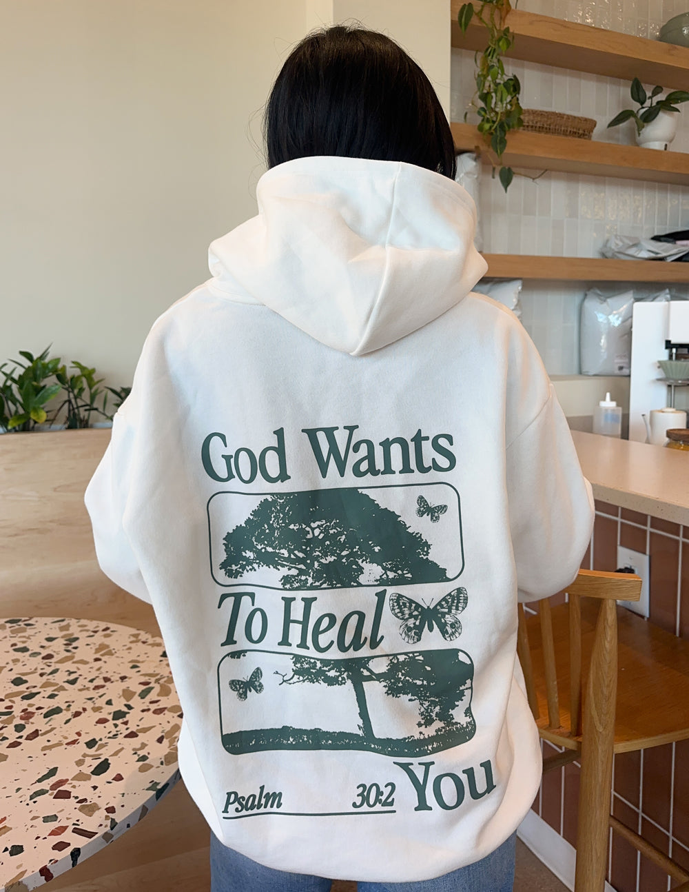 White unisex hoodie with large green back graphic reading God Wants To Heal You