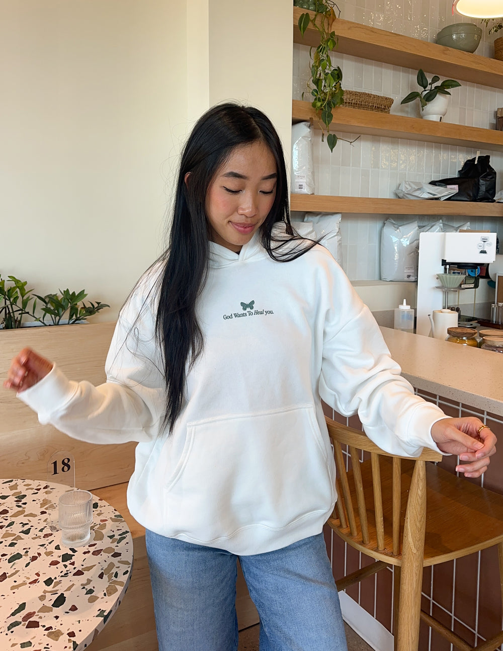 White unisex hoodie with small green chest text logo and front pouch pocket