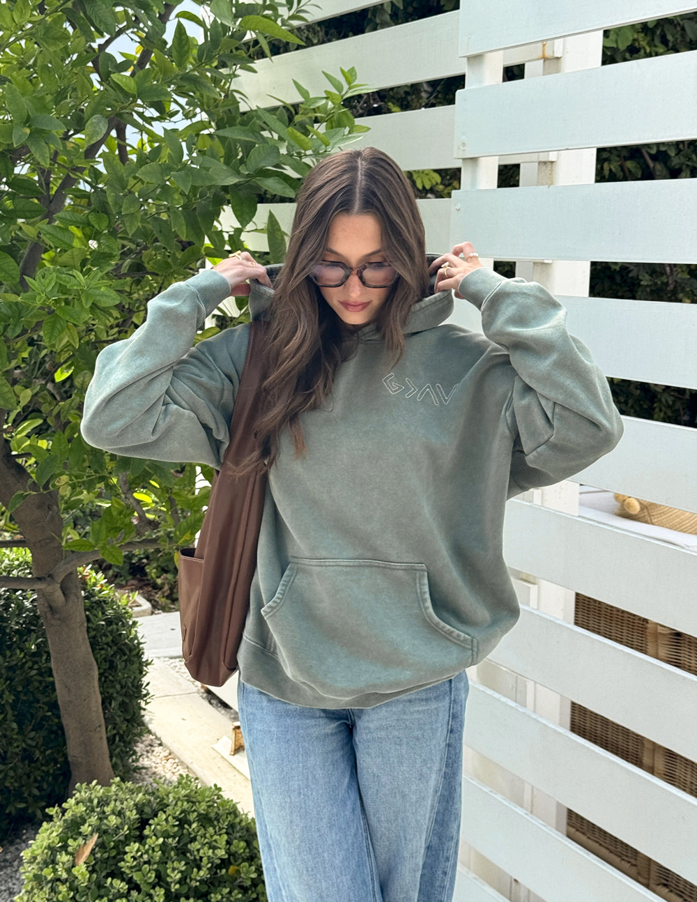 Sage green unisex hoodie with pullover hood and front pocket, hands in sleeves