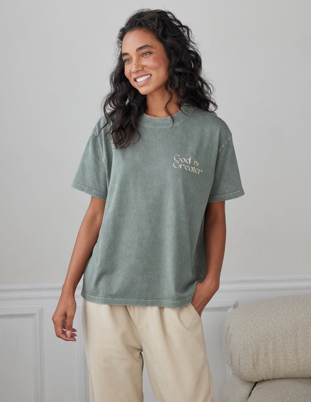Unisex graphic tee in sage green with small “God is Greater” print on the chest