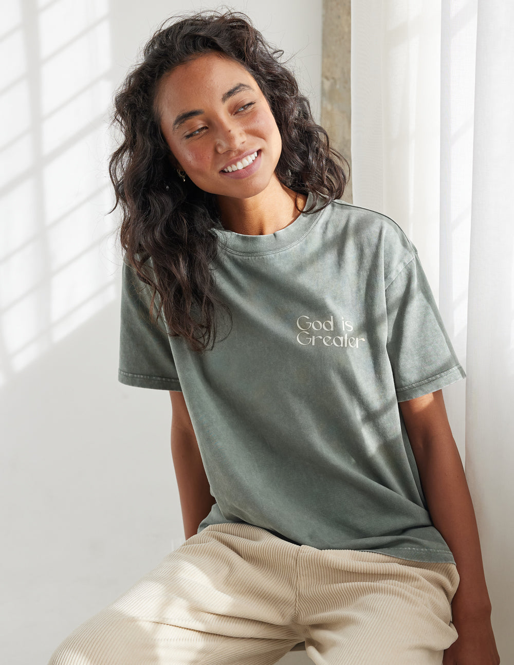 Unisex graphic tee in sage green with “God is Greater” text print on the chest