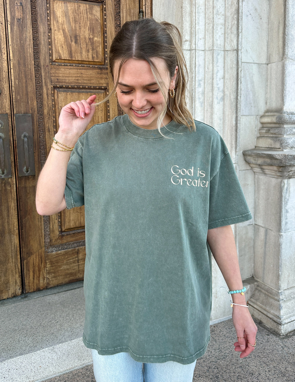 Unisex graphic tee in sage green with “God is Greater” print on the chest