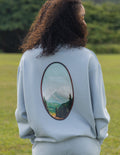 Light blue unisex crewneck sweatshirt with oval landscape graphic on back