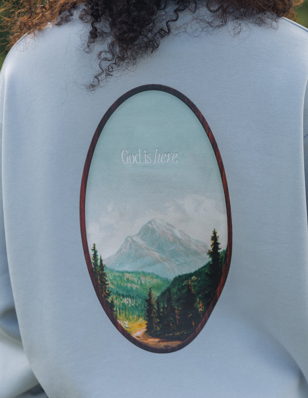 Light blue unisex crewneck sweatshirt with oval landscape graphic on chest