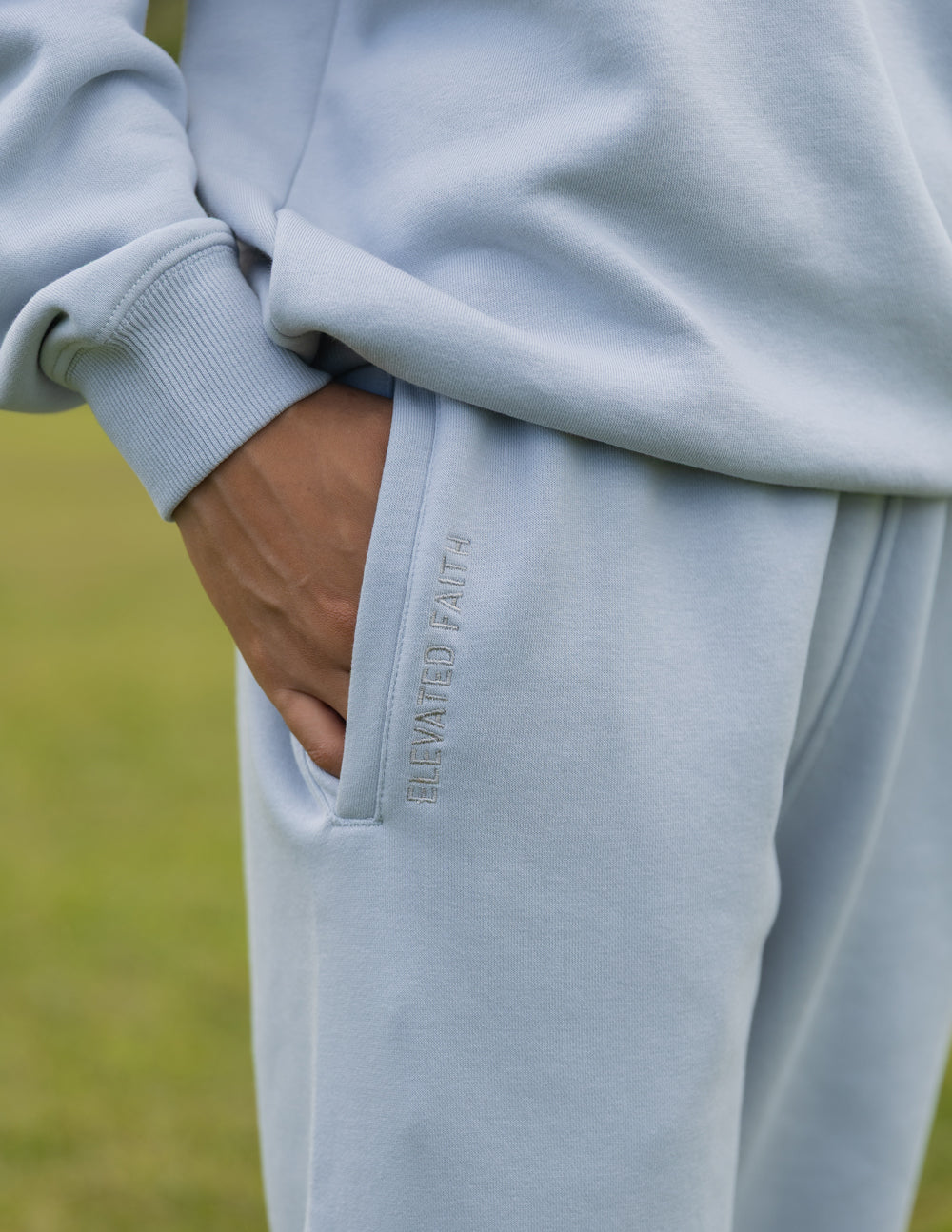 Light blue sweatpants with side pocket and vertical 'God is here' embroidery