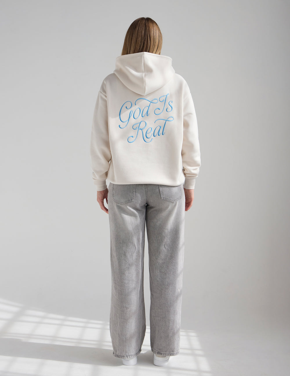 Unisex off-white hoodie, back view, blue “God Is Real” text and hood