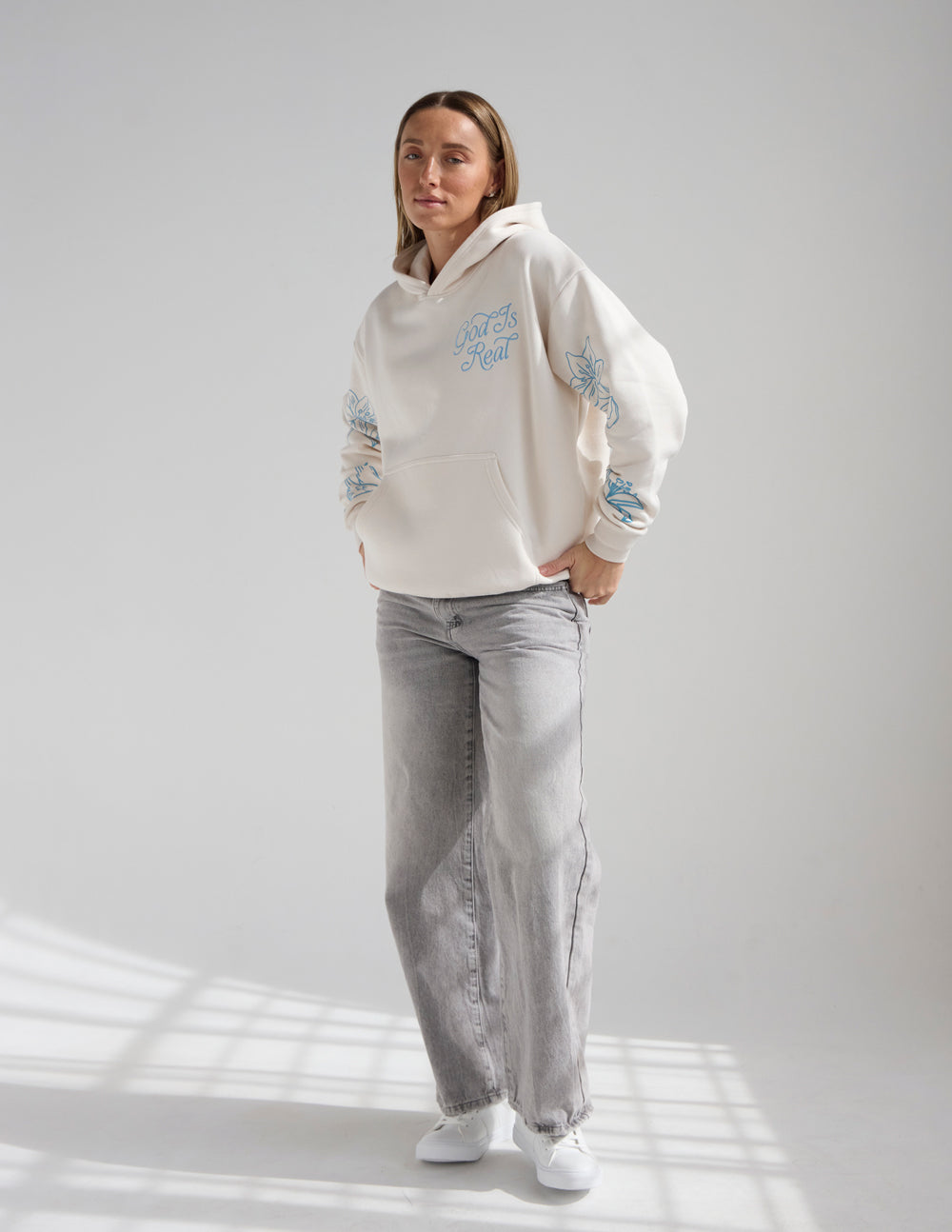 Unisex off-white hoodie with blue “God Is Real” chest print, front pocket