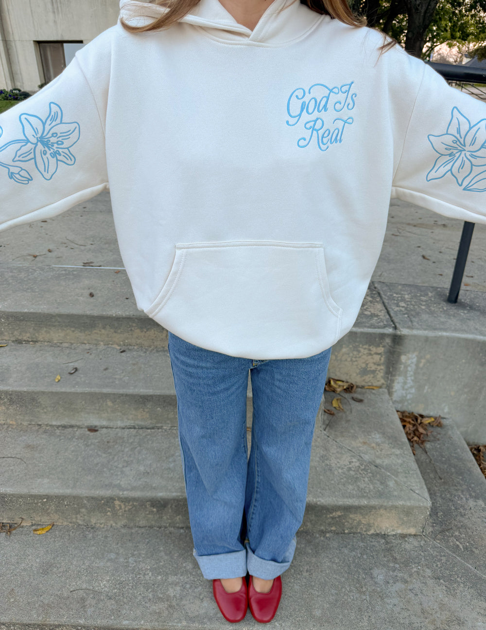 Unisex off-white hoodie with front pocket, blue “God Is Real” chest print