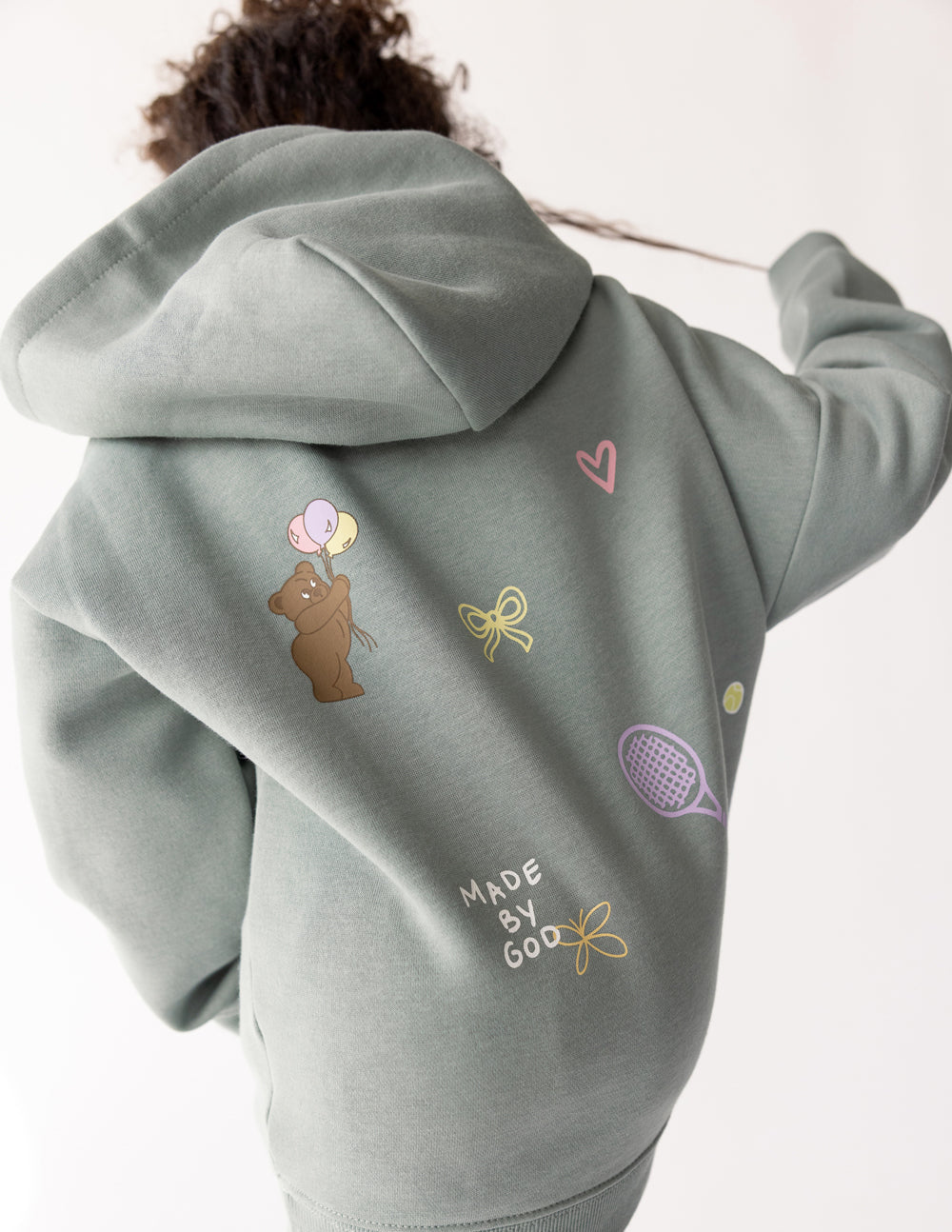 Kids sage green hoodie back view with colorful icons and "Made by God" text.