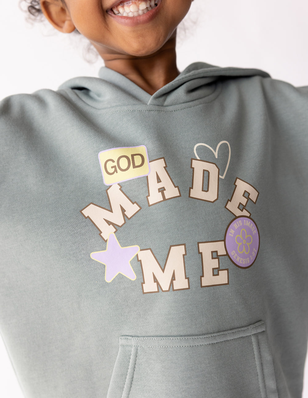 Kids sage green hoodie with large "GOD MADE ME" chest graphic and heart icon.