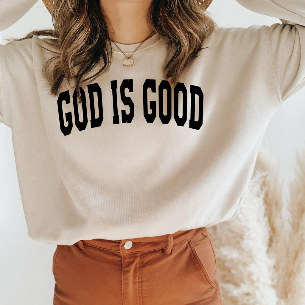 Unisex crewneck sweatshirt in light peach with "GOD IS GOOD" front graphic